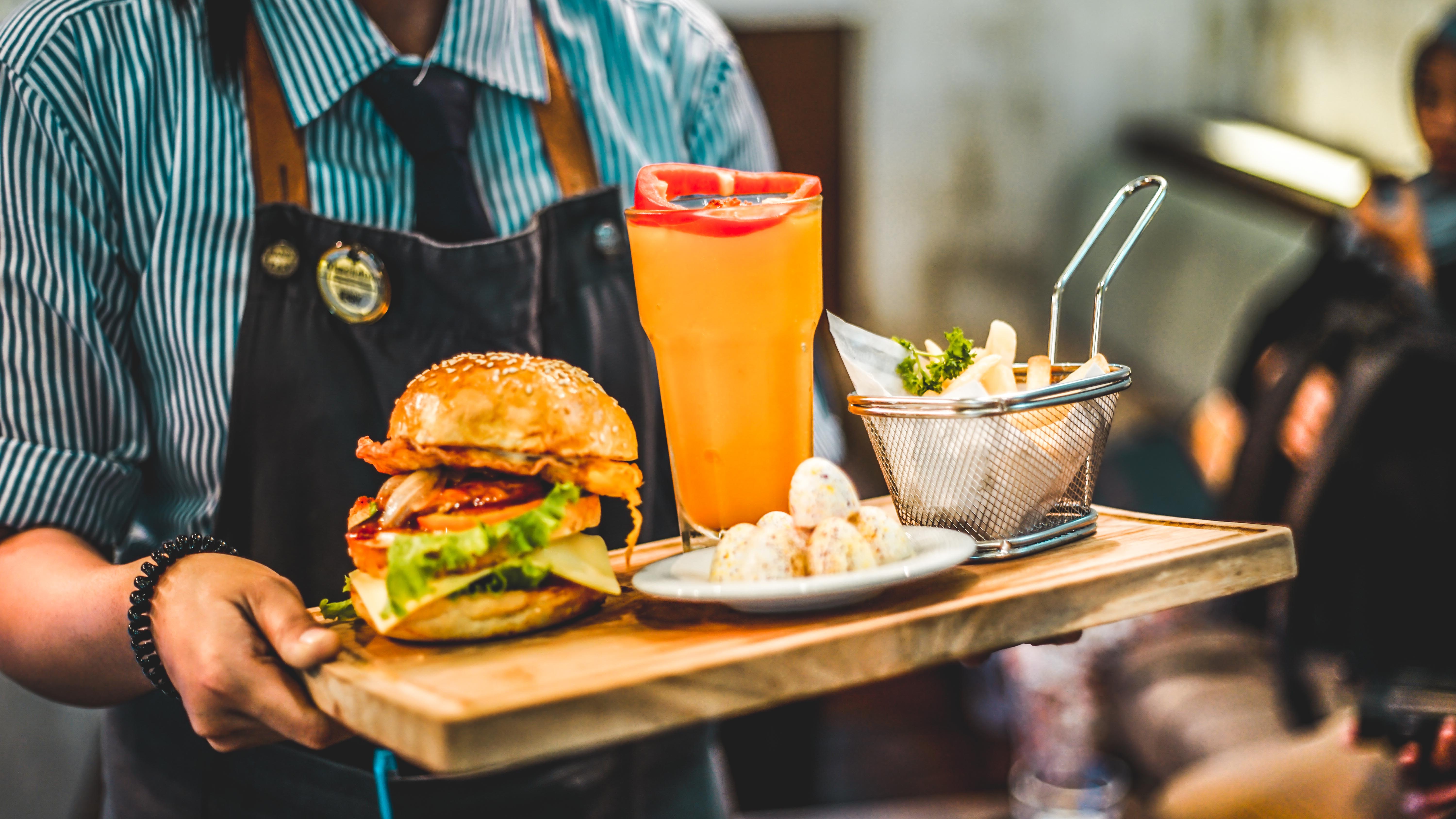 Číšník v pruhované košili a zástěře nese hamburger a pití